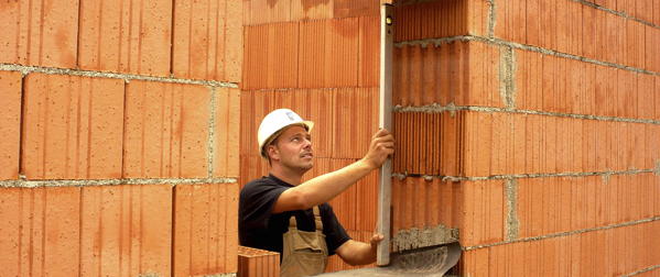 Bauarbeiter mit Richtlatte prüft Mauerwerk