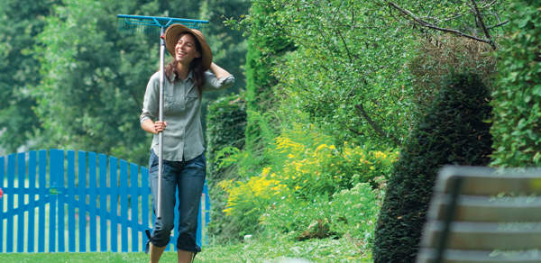 Frau mit Rechen macht Pause bei der Gartenarbeit