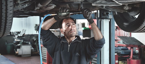 (Foto: Mann arbeitet mit Druckluft-Ratschenschrauber unter einem Auto) 