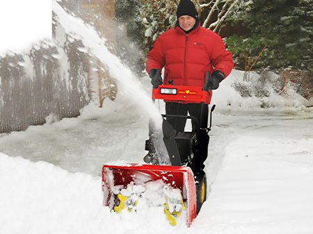 Mann räumt mit motorisierter Schneefreäse Schnee auf dem Hof