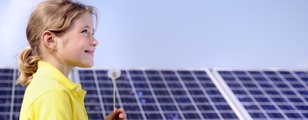 Foto: Kind mit Pusteblume vor Solarpaneelen
