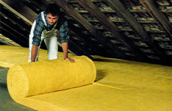 Mann rollt Dämnmstoff auf einer Geschossdecke im Dach aus