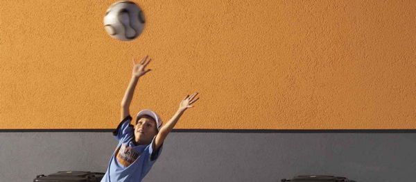 Foto: Junge springt vor einer Hausfassade nach seinem Fußball