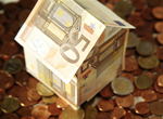 Haus aus Geldscheinen steht auf Euro-Münzen