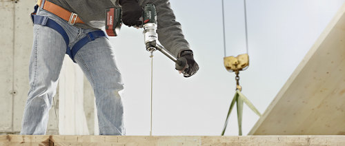 Mann auf Baustellen schraubt Balken mit Akkuschrauber