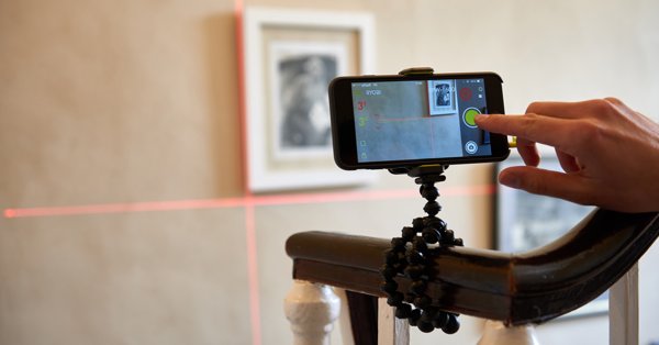 (Foto: Smartphone mit Kreuzlinienlaser beim Ausmessen einer Wand) 